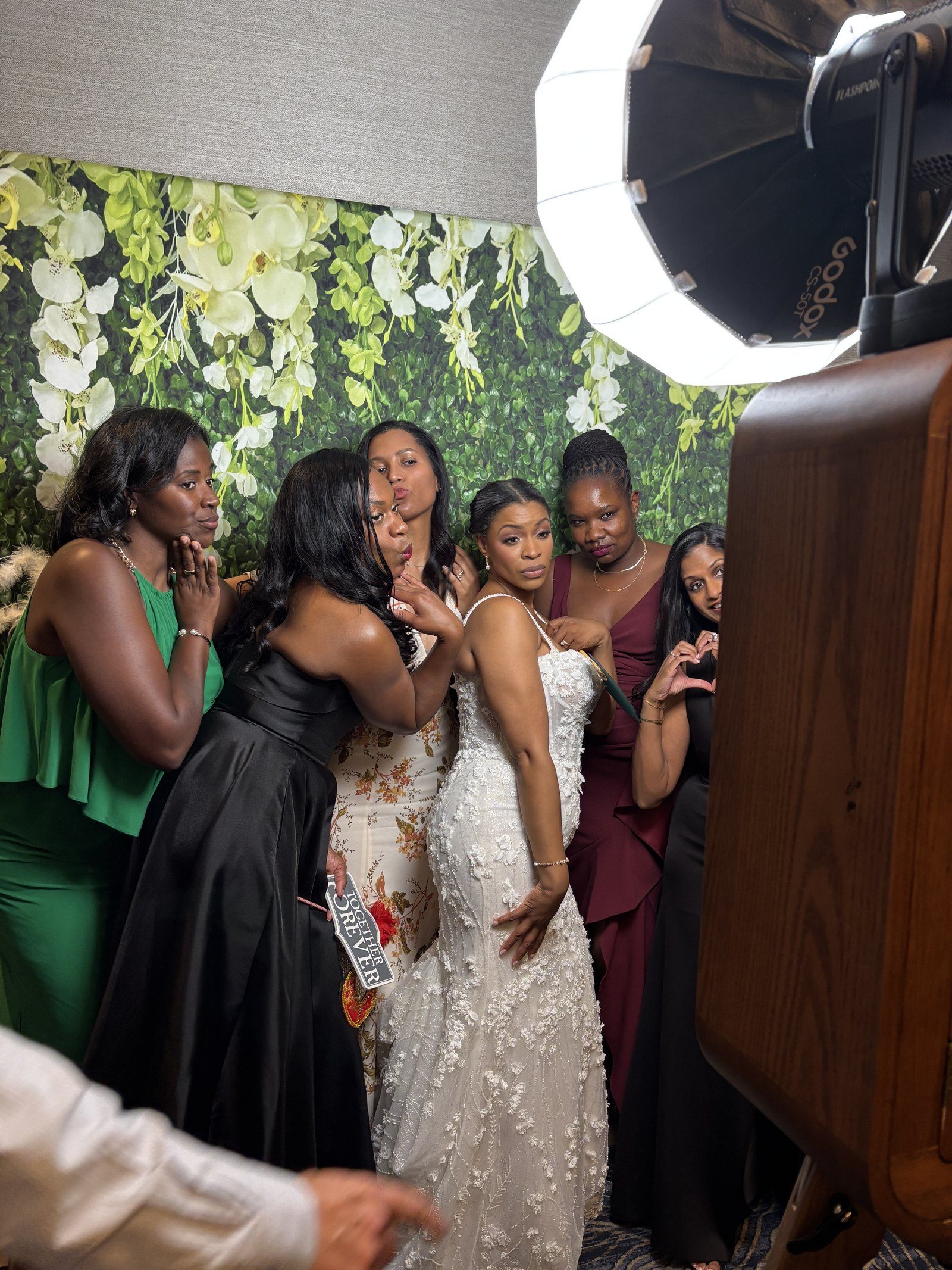 A bride and her bridesmaids posing together with props at the Ikonic vintage photo booth
