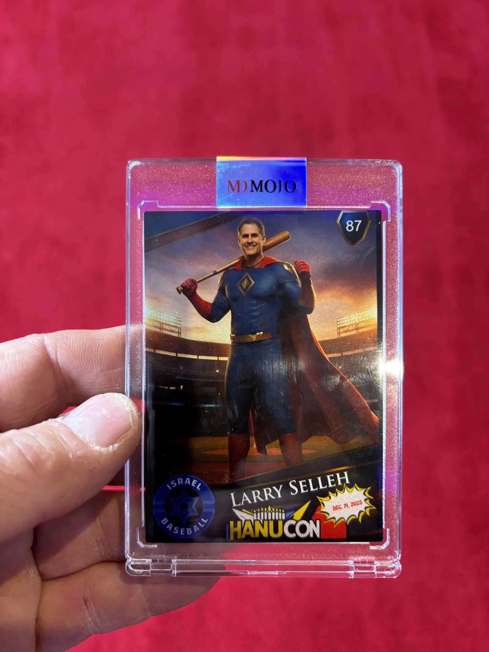 A finished trading card in an MD Mojo slab held up at an event, showing a guest styled as a comic-book hero